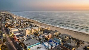 Vista aérea de un pueblo costero con edificios a lo largo de la playa, una carretera que discurre paralela a la orilla, y el océano al fondo.