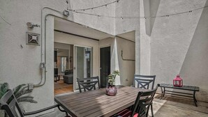 Um pátio com mesa e cadeiras de madeira, um vaso de planta e um lanterna vermelha.