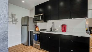 Uma cozinha moderna com armários pretos, eletrodomésticos de aço inoxidável e piso de madeira.