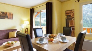 A dining area with a table set for two, a bowl of fruit, and a basket of bread on the table. - Chalet in Isola with Scenic Views (LE HAMEAU)