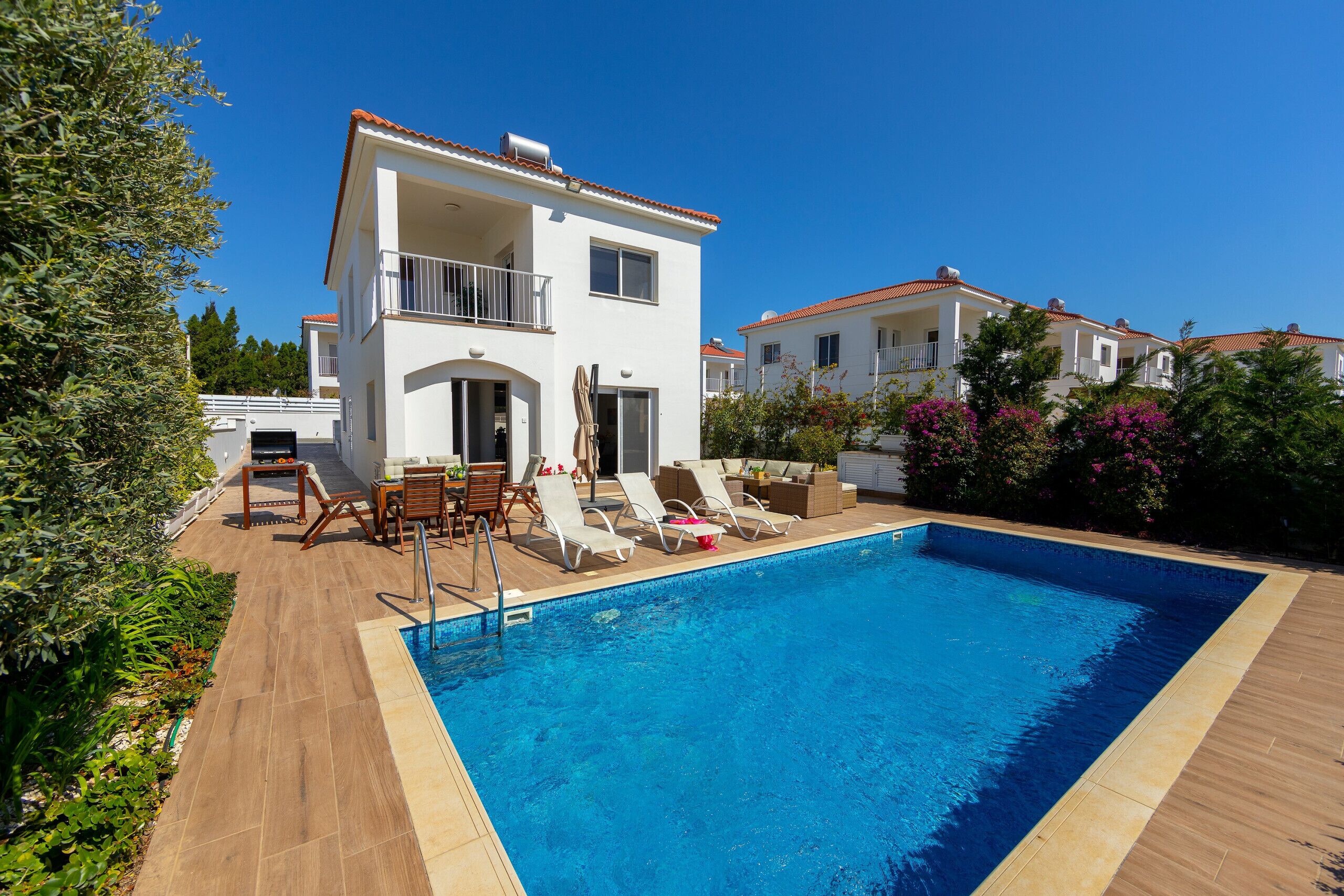 A two-story building with a swimming pool, outdoor furniture, and a garden.