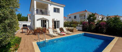 A two-story building with a swimming pool, outdoor furniture, and a garden.