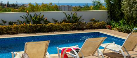 A poolside area with two lounge chairs, a tiled pool, and a view of the sea.
