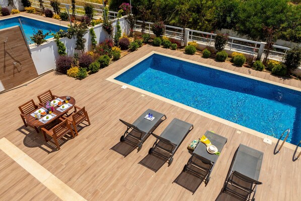 A rooftop pool area with a wooden deck, a dining table with chairs, and lounge chairs. - Napa Bay View Villa 3 (Ayia Napa)