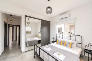 A modern bedroom with a large bed, a bedside table, a mirror, and a wardrobe. - Napa Bay View Villa 3 (Ayia Napa)