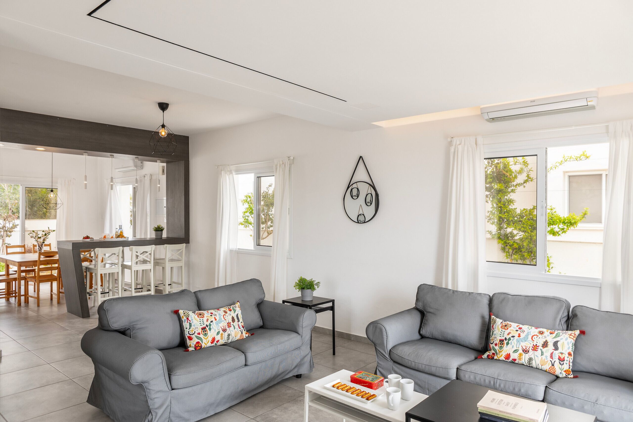 A modern living room with two grey sofas, a coffee table, and a dining area with a white table and chairs.