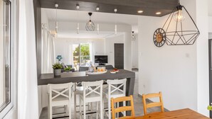Una cocina moderna con encimera oscura, sillas blancas e iluminación colgante.