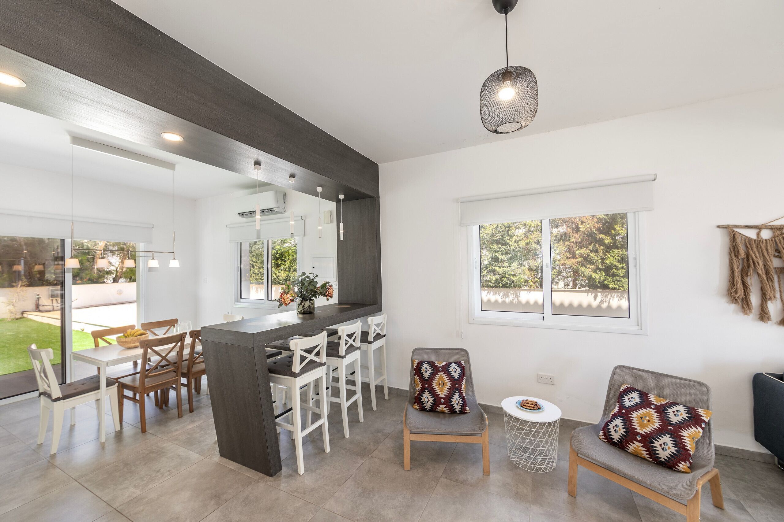 A modern kitchen with a dark countertop, white chairs, and a large window.