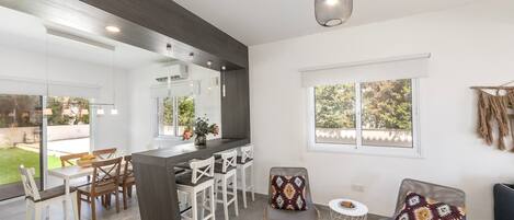 A modern kitchen with a dark countertop, white chairs, and a large window.