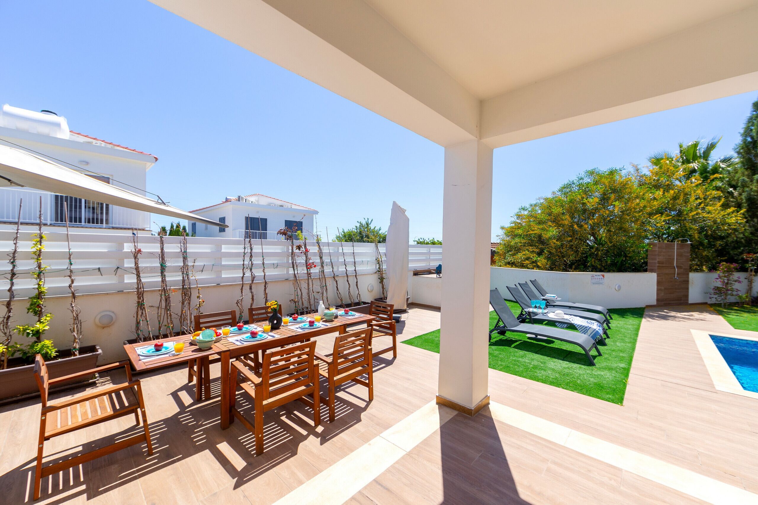 Eine überdachte Terrasse mit Esstisch, Stühlen und einem Poolbereich mit Liegestühlen.