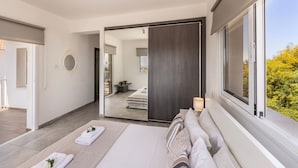 Quarto moderno com uma cama grande, porta deslizante para um banheiro e vista para o exterior.