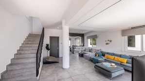 Uma sala de estar moderna com escada, piso de azulejos cinza, um sofá cinza com almofadas amarelas e uma TV de tela plana.