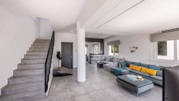 Una sala de estar moderna con una escalera, suelo de baldosas grises, un sofá gris con cojines amarillos y un televisor de pantalla plana.
