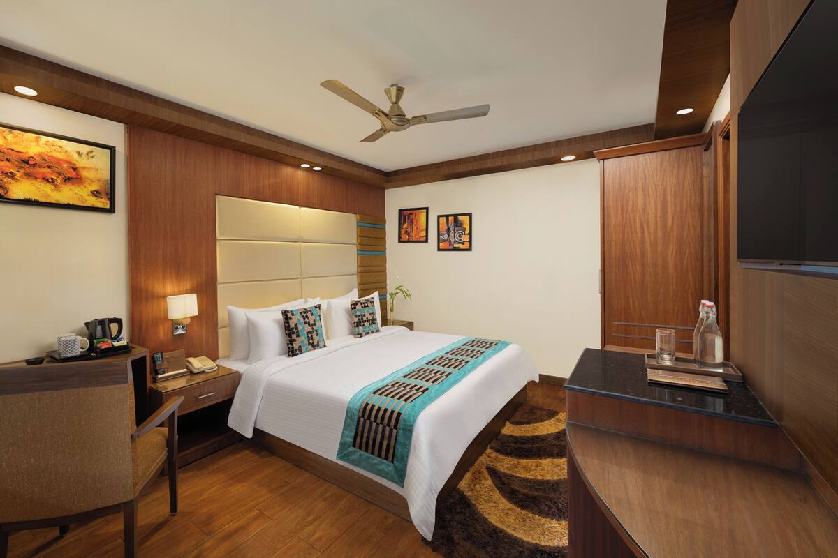 Une chambre d’hôtel avec un grand lit, un bureau, une chaise, une télévision et un ventilateur de plafond.