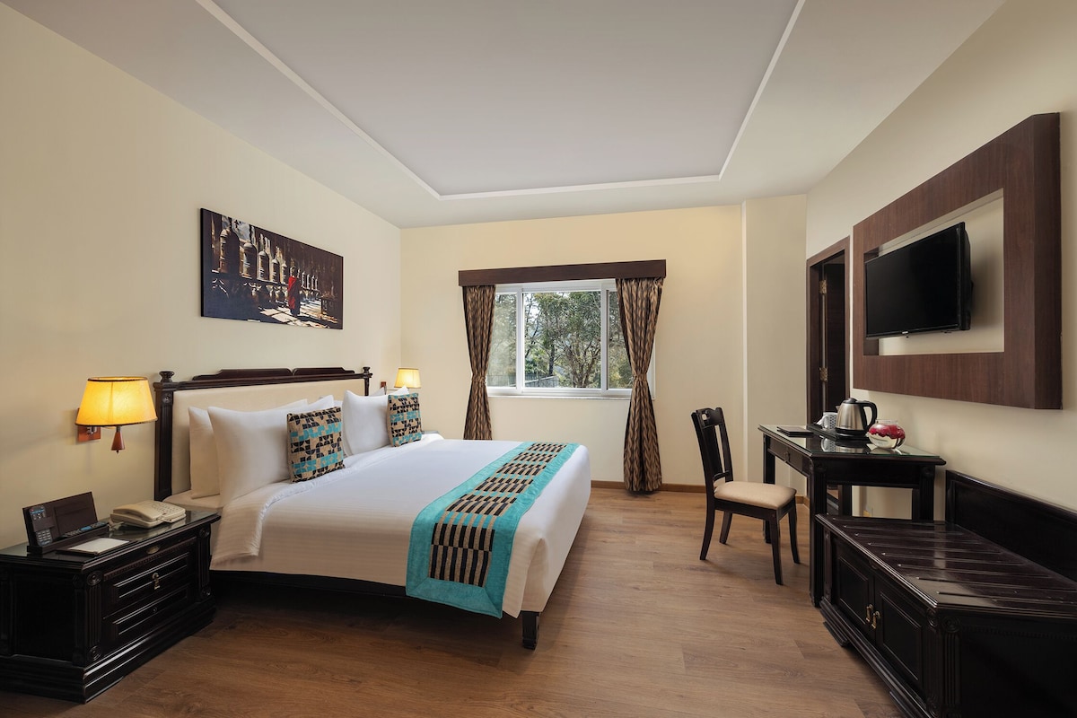 A hotel room with a bed, bedside table, lamp, TV, and a window with curtains.