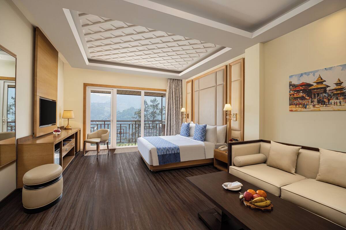 Une chambre d’hôtel avec un lit, un canapé, un bureau avec une lampe, une télévision et un panier de fruits.