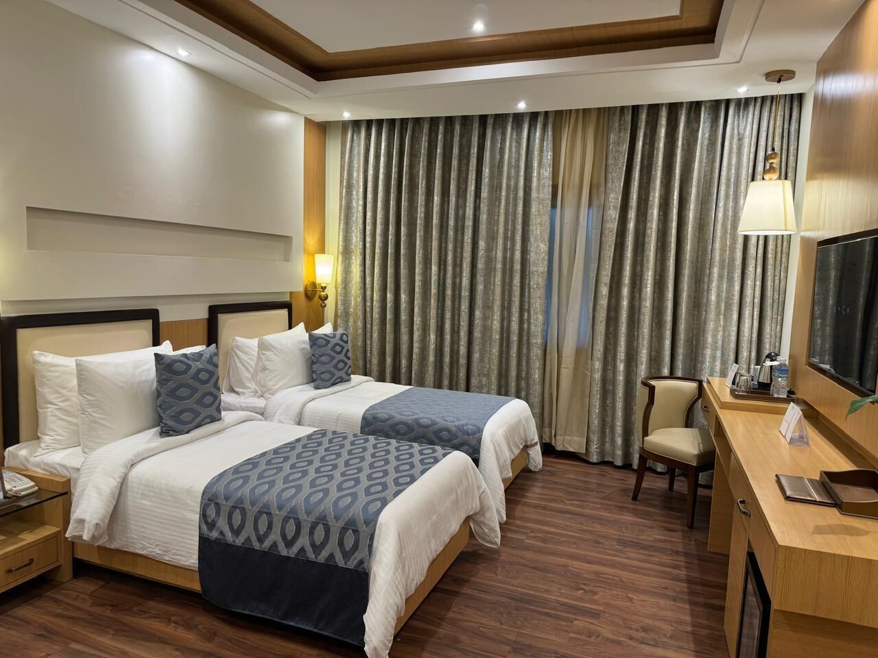 A hotel room with two beds, a desk, a chair, and a television.