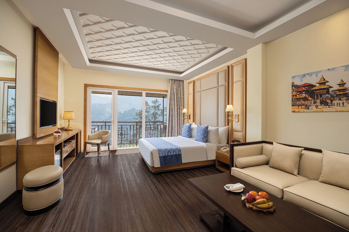 A hotel room with a bed, a sofa, a desk with a lamp, a TV, and a fruit basket.