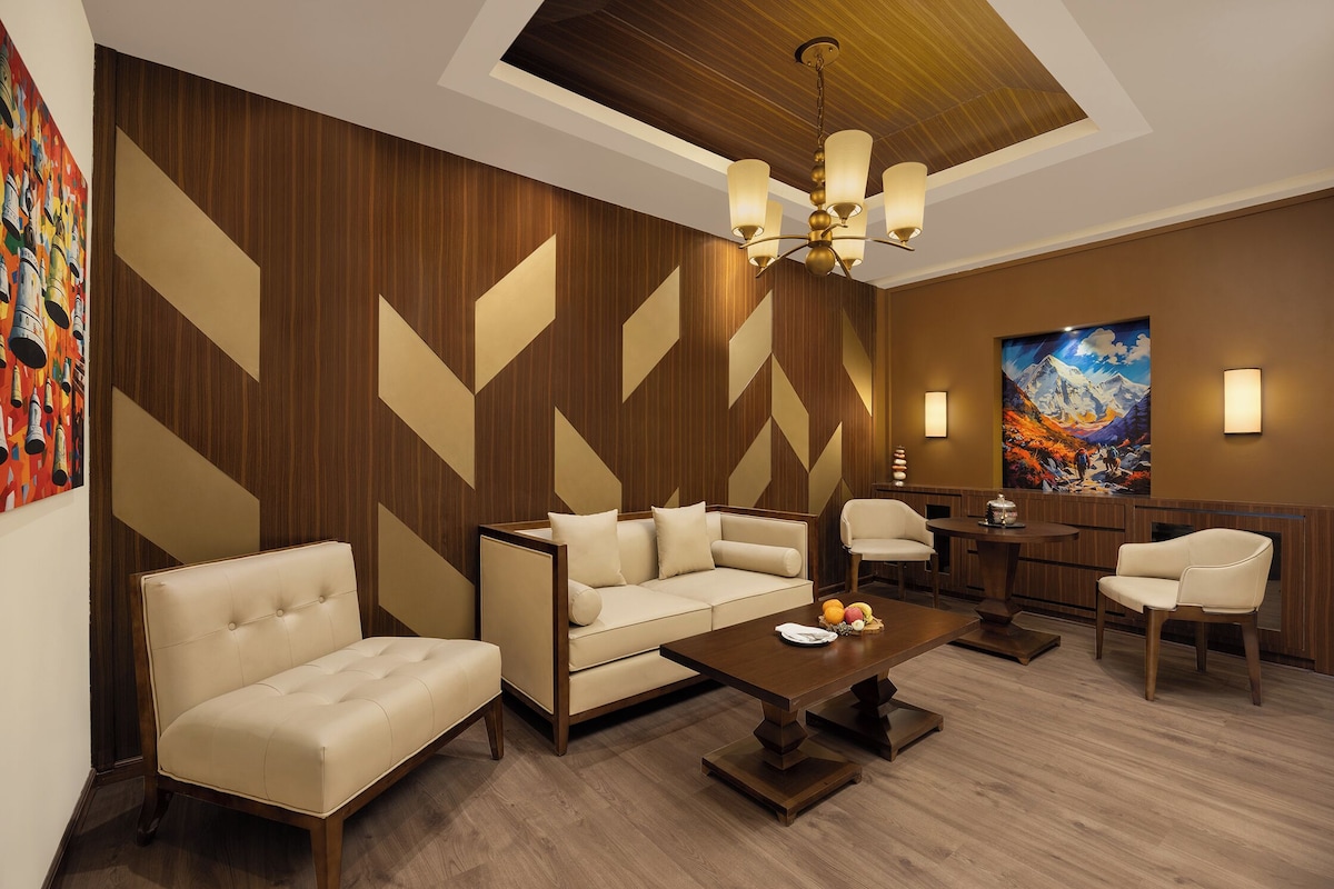 A modern living room with a sofa, coffee table, and chairs, wooden panel walls, and a painting on the wall.