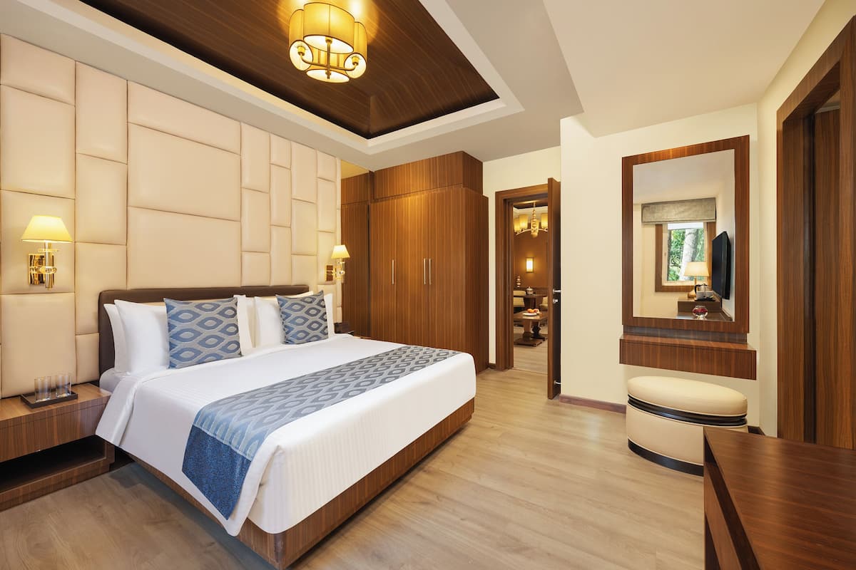 Une chambre d’hôtel moderne avec un grand lit, une armoire en bois, des lampes de chevet, un miroir et un petit coin salon.