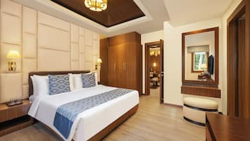 A modern hotel room with a large bed, wooden wardrobe, bedside lamps, a mirror, and a small seating area.