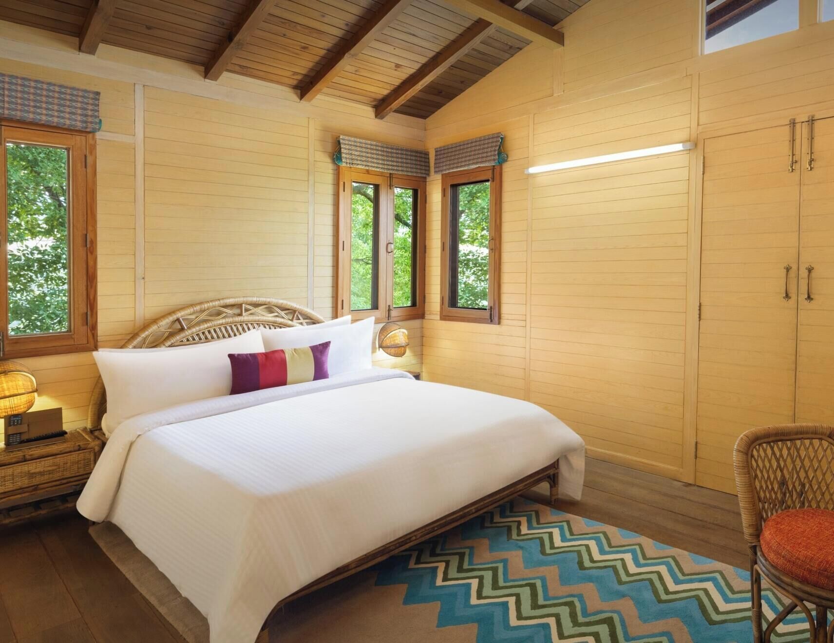 Una habitación de madera con una cama, una silla y un armario. Hay ventanas y una lámpara.