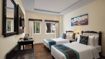 A hotel room with two beds, a desk, a mirror, a painting, and a window with curtains.