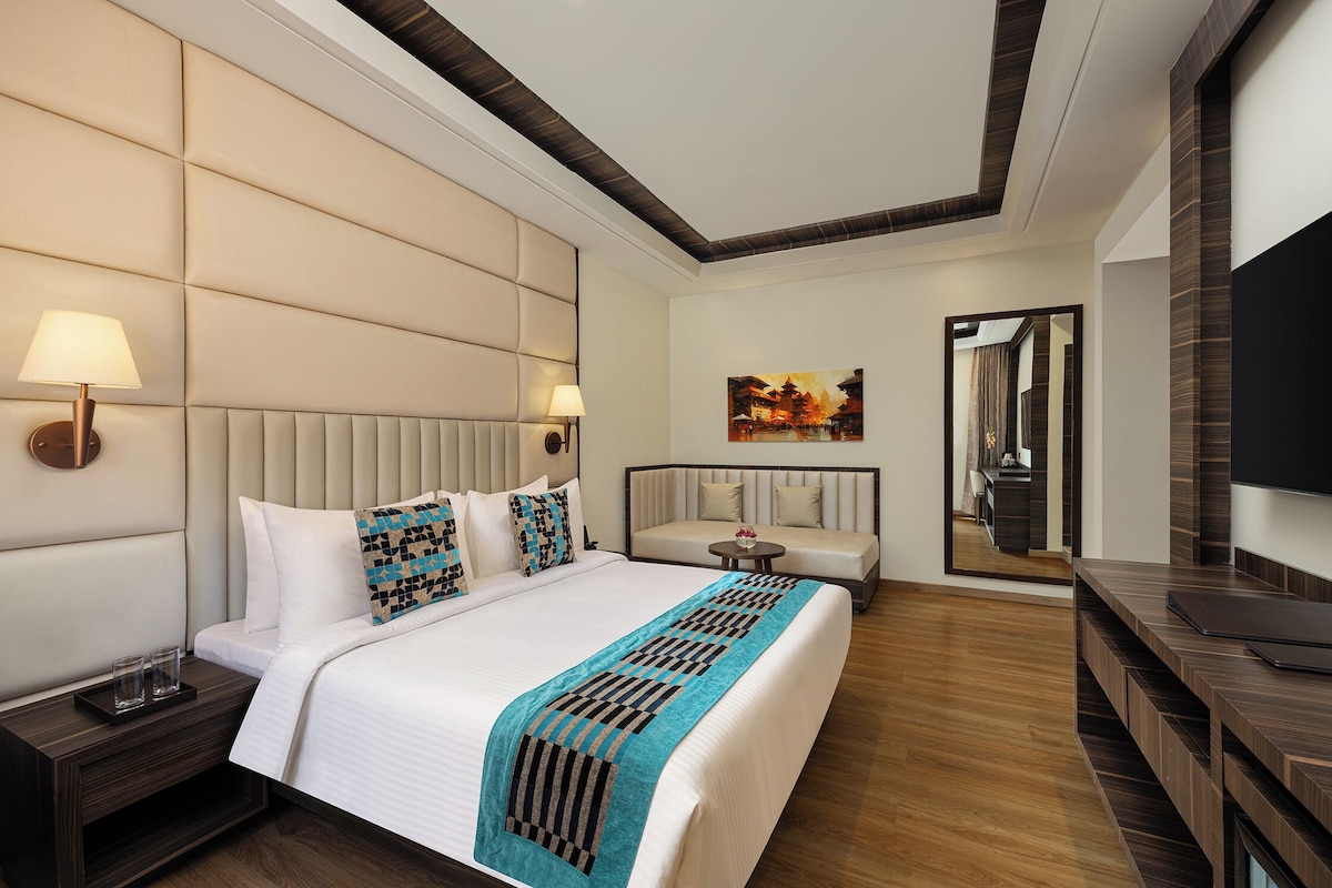 A hotel room with a large bed, a sofa, a TV, and a painting on the wall.