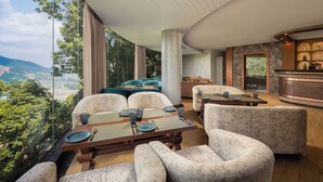 A modern dining area with a panoramic view, featuring a large table with chairs, a bar area with bottles, and a seating area with sofas. - Fortune Resort & Wellness Spa Bhaktapur, Nepal - Member ITC Hotels' Group (Suryabinayak)