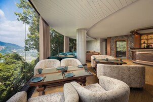 Un comedor moderno con vistas panorámicas, que cuenta con una gran mesa con sillas, una zona de bar con botellas y un área de estar con sofás.