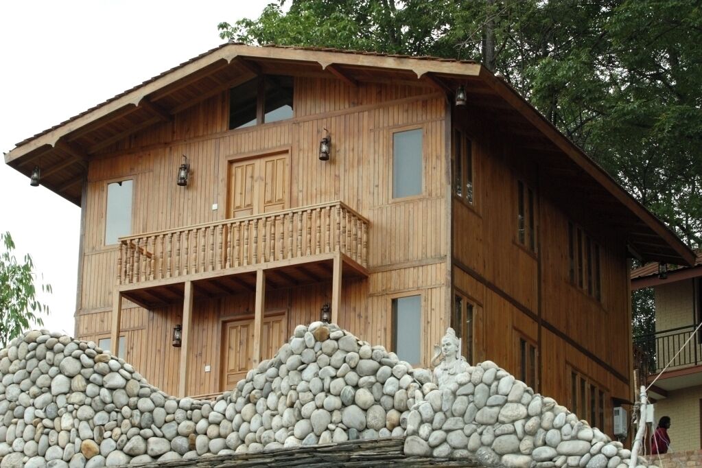 Un edificio de madera de varios pisos con un balcón, un muro de piedra en primer plano y una estatua.