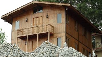 Un edificio de madera de varios pisos con un balcón, un muro de piedra en primer plano y una estatua.