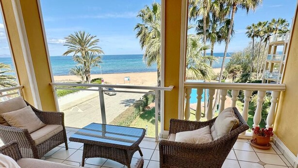 Un balcón con mobiliario de mimbre, vista a la playa y palmeras.