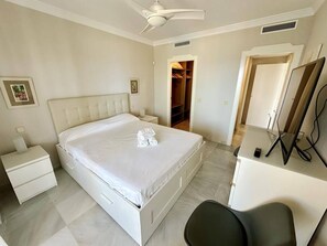 A bedroom with a bed, bedside tables, a desk, a chair, a wardrobe, and a ceiling fan.