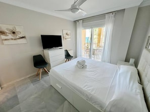 Un dormitorio con cama, televisión, sillón y ventana con cortinas.