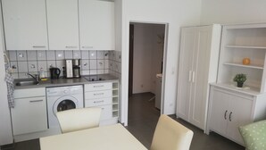 A compact kitchen with a washing machine, a coffee maker, and a sink. There is a dining table with chairs and a small shelf with a plant. - Ruhige Ferienwohnung/ Amateurzimmer/ Gute Verkehrsanbindung (Linden)