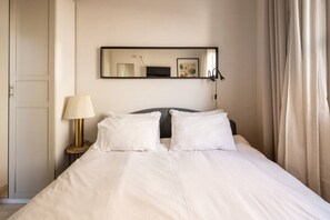 Ett hotellrum med en säng, en sänglampa, en spegel och en dörr.
