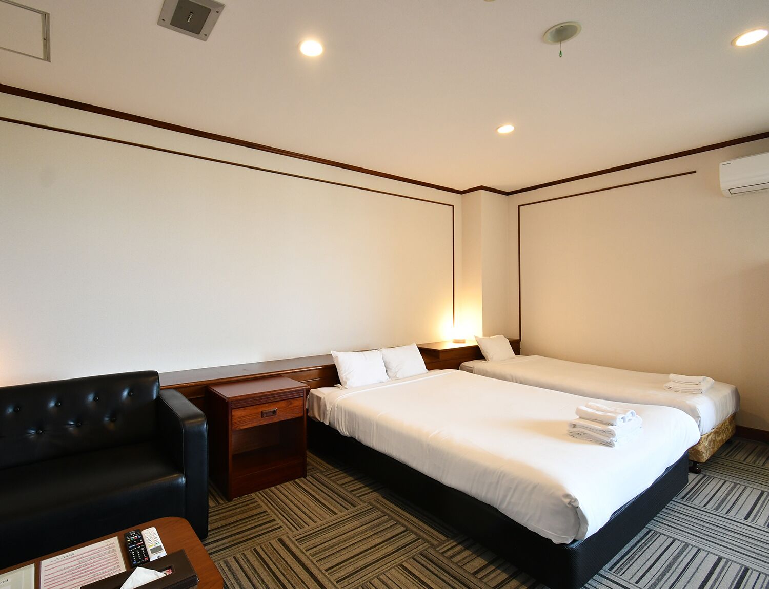 Quarto de hotel com duas camas, uma escrivaninha, uma cadeira e uma mesa de cabeceira.