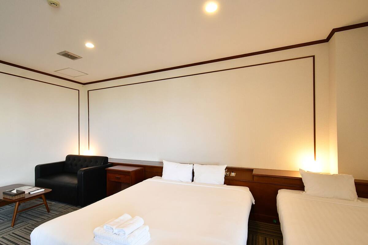 Quarto de hotel com uma cama grande, uma poltrona pequena, uma escrivaninha com luminária e televisão na parede.