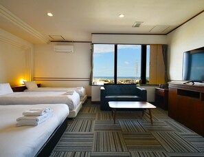 Ein Hotelzimmer mit zwei Betten, einem Schreibtisch, einem Fernseher und Blick auf die Stadt.