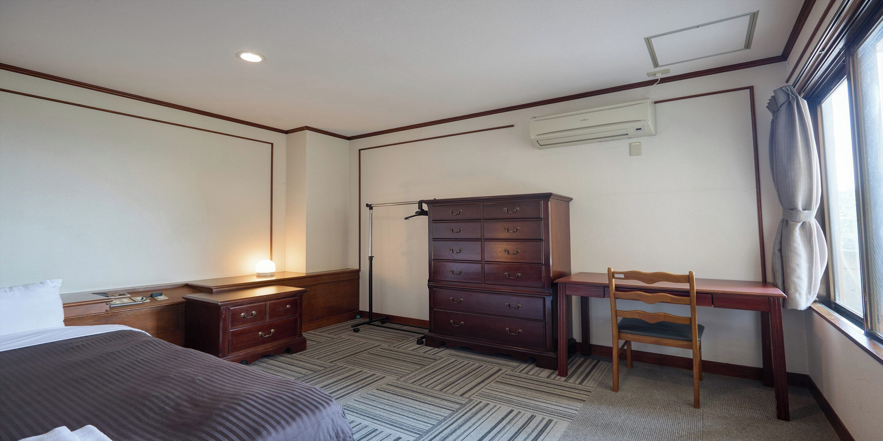 A hotel room with a bed, a desk, a chair, a dresser, and a window with curtains.