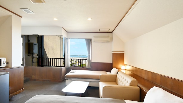 A hotel room with a bed, a sofa, a small table, and a balcony with a view. - Purari (Okinawa)