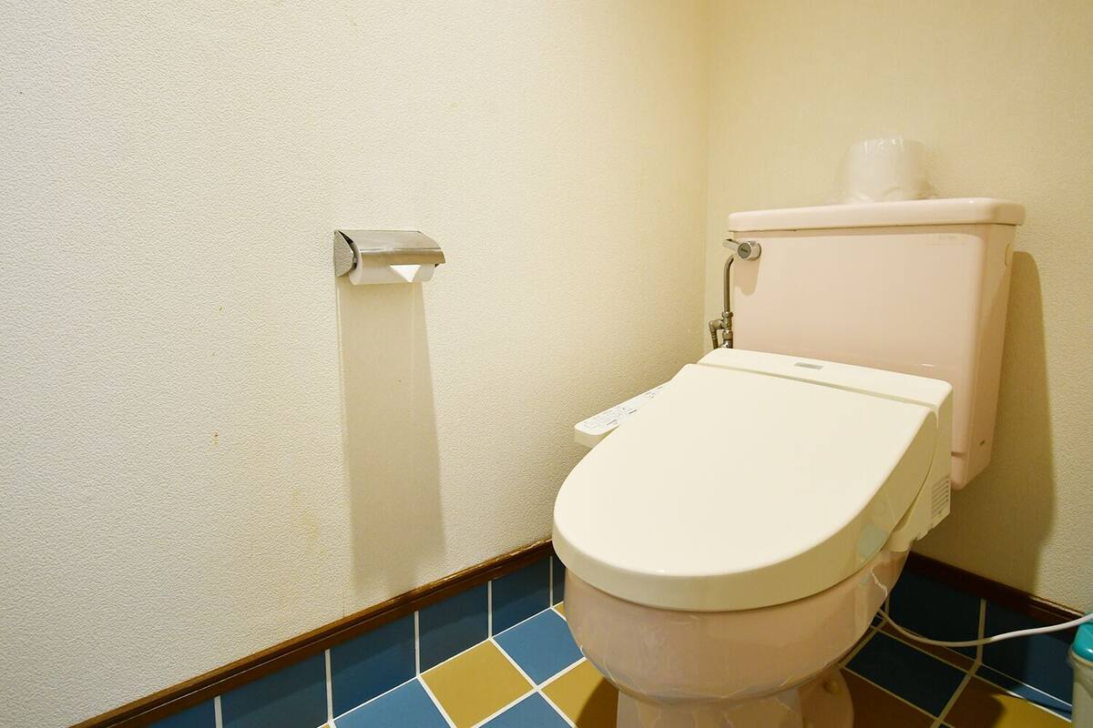 Um banheiro pequeno com vaso sanitário, dispensador de papel toalha e piso revestido de azulejos.