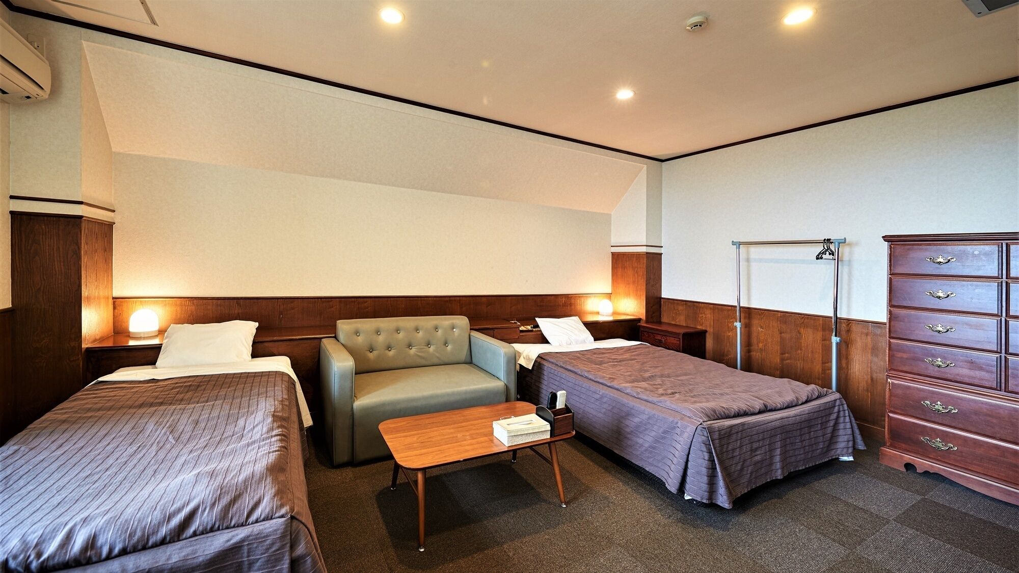 A hotel room with two single beds, a sofa, a wooden dresser, and a small table.