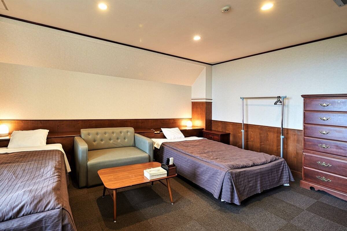 Quarto de hotel com duas camas de solteiro, um sofá, uma cômoda de madeira e uma mesa pequena.