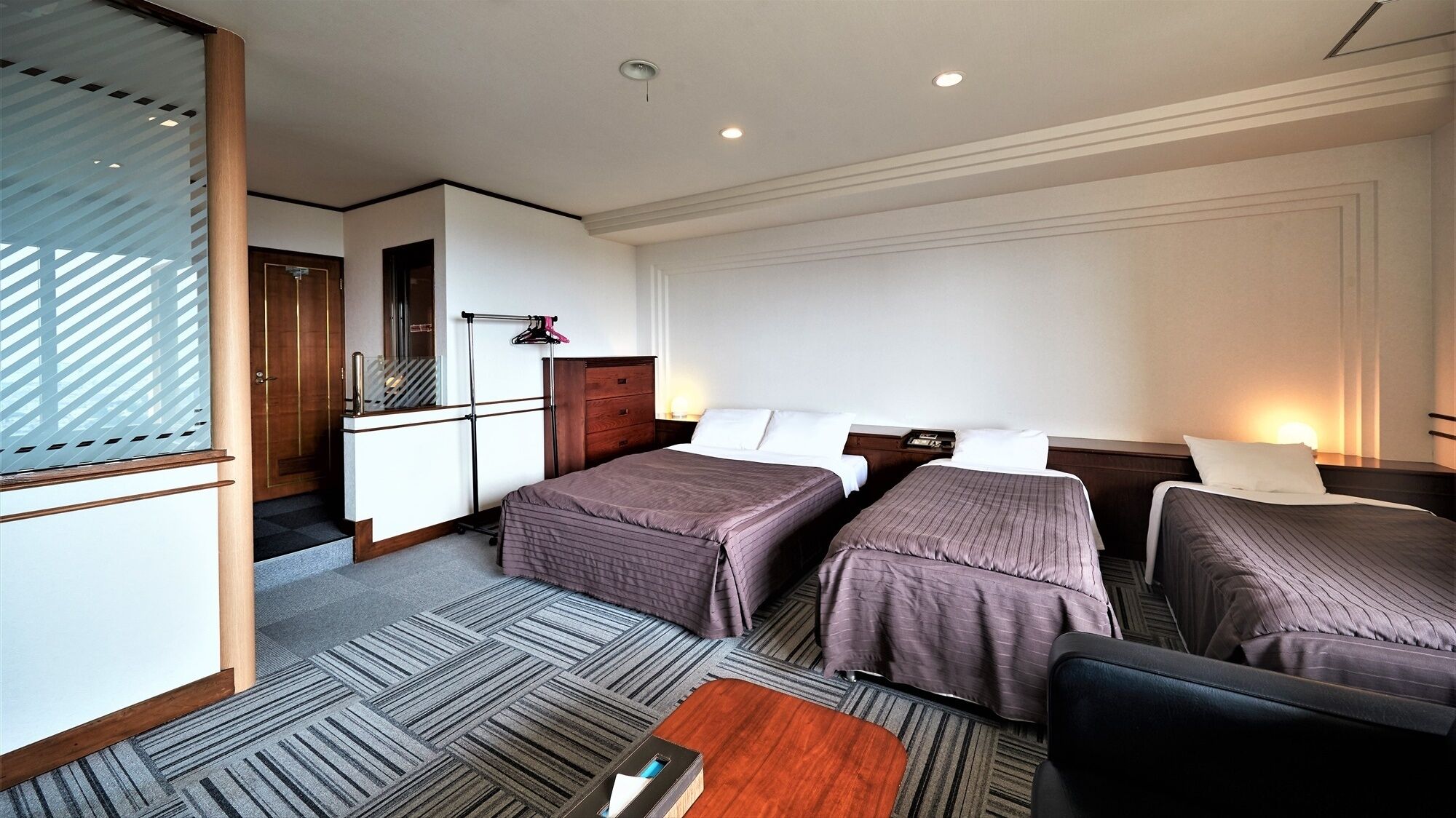 A hotel room with two beds, a desk, a chair, and a small table.