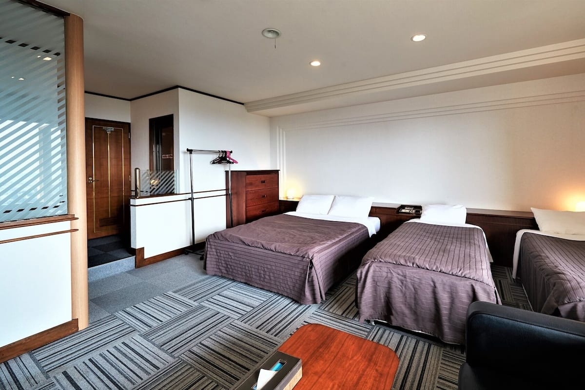 Quarto de hotel com duas camas, uma mesa, uma cadeira e uma mesinha.