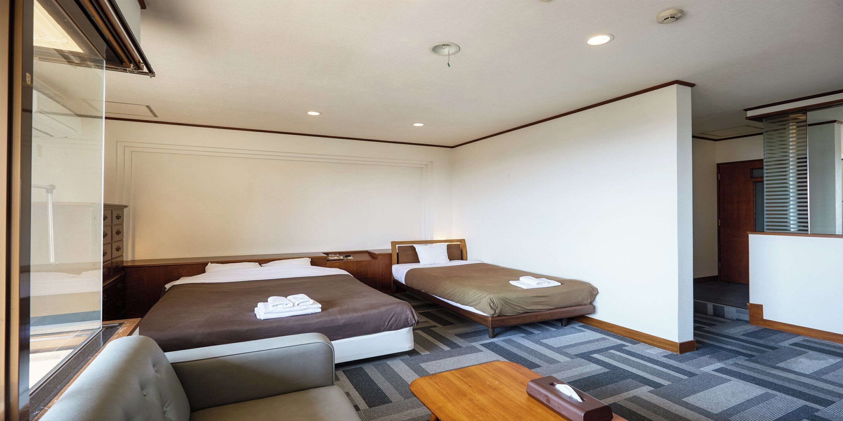 A hotel room with two beds, a sofa, a small table, and a window with blinds.