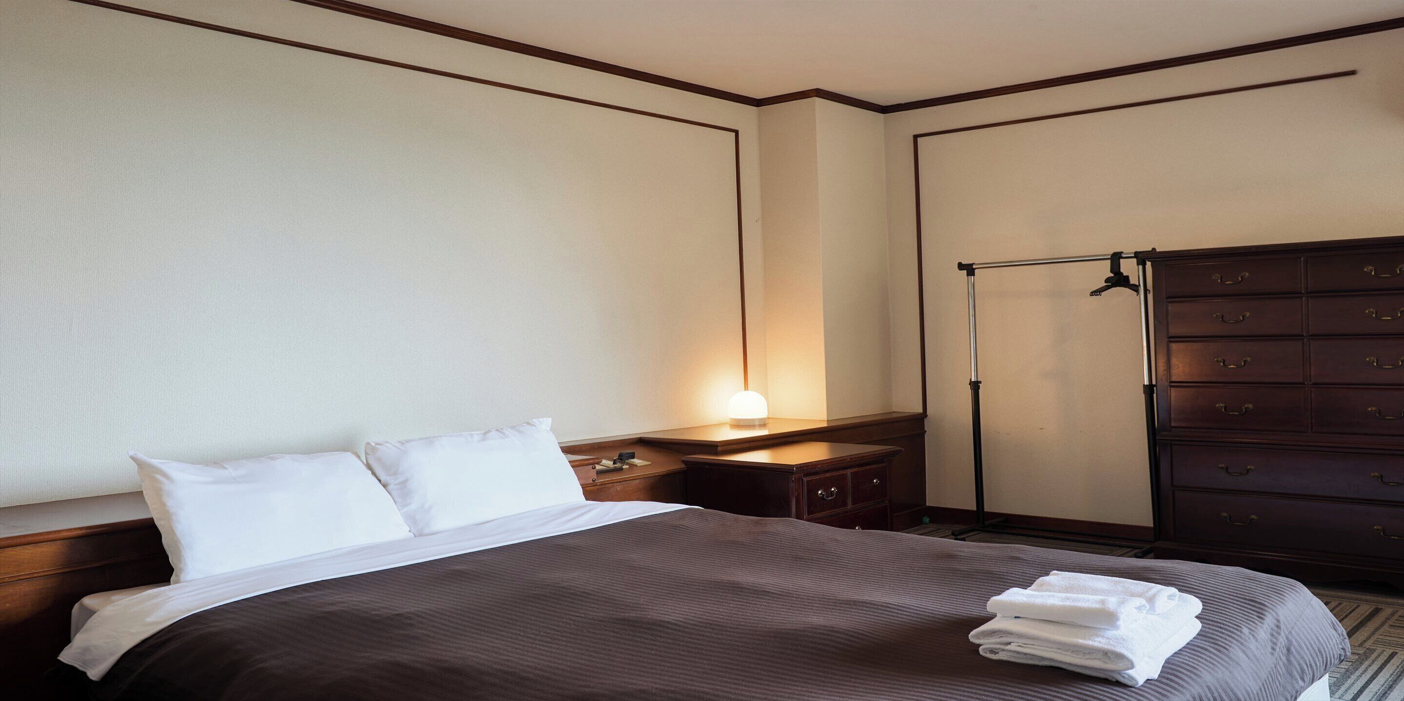 Une chambre d’hôtel avec un grand lit, une commode, une table de chevet et une lampe fixée au mur.