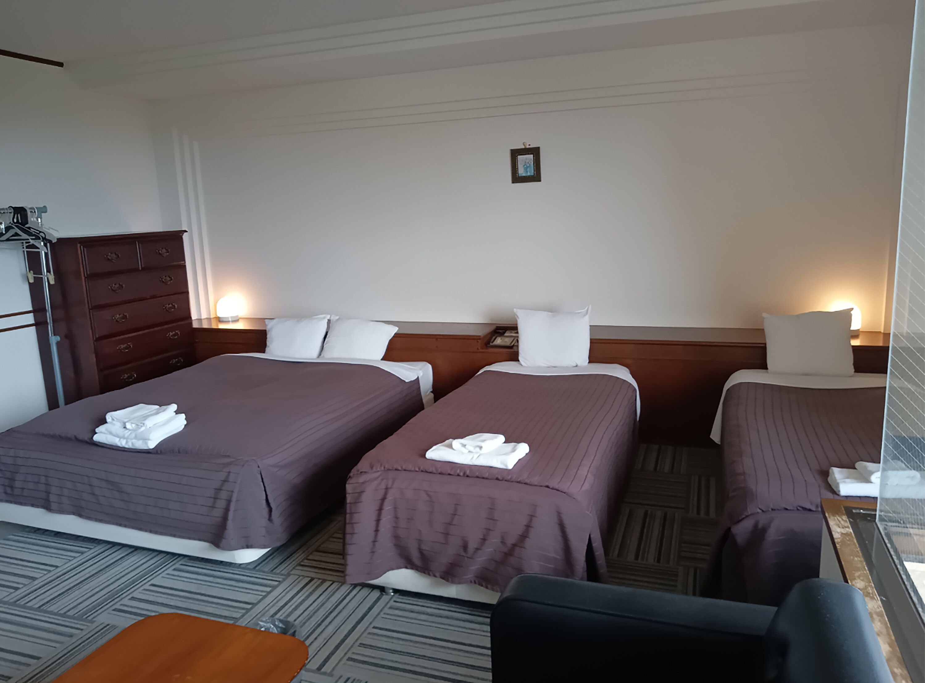 A hotel room with two beds, a wooden dresser, a small table, and a chair.